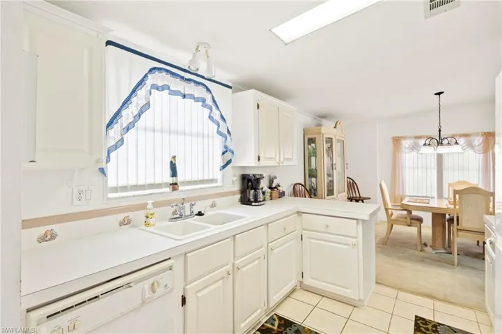 Kitchen with white dishwasher, a sink, light tile patterned floors, light carpet, and visible vents