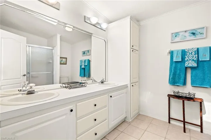 Bathroom with a shower stall, crown molding, a sink, double vanity, and tile patterned flooring