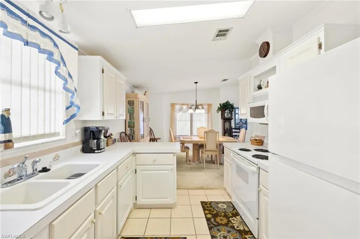 Kitchen featuring a peninsula, a sink, visible vents, an inviting chandelier, and white appliances
