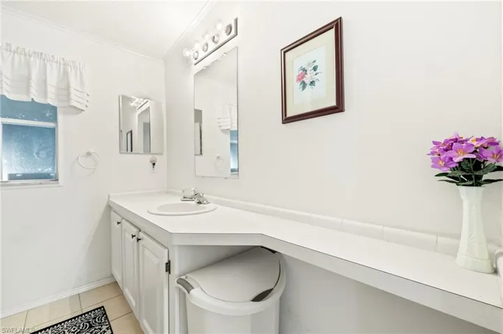 Bathroom with vanity, baseboards, ornamental molding, and tile patterned flooring