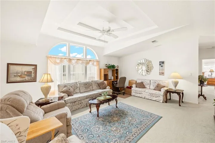 Carpeted living area with a ceiling fan and a tray ceiling