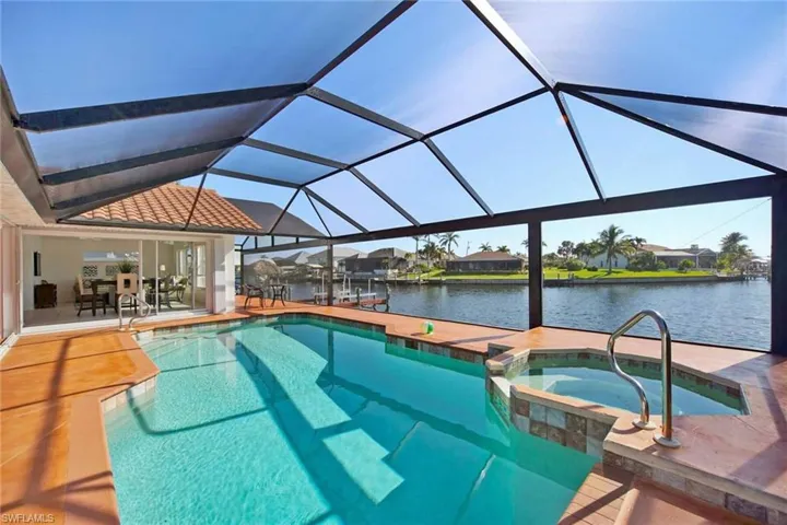 View of pool featuring a patio, a water view, a pool with connected hot tub, and glass enclosure