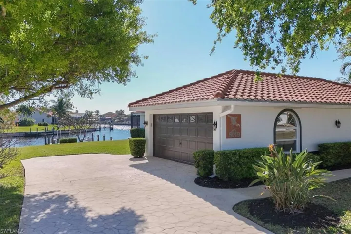 View of property exterior featuring a tile roof, driveway, stucco siding, an attached garage, and a water view