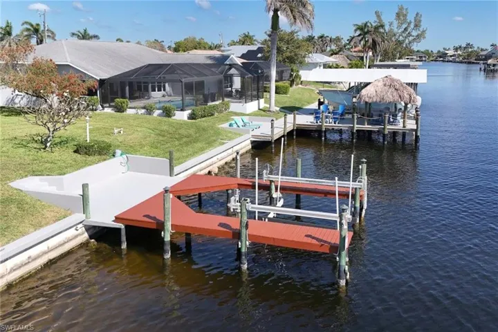 Dock area with a lawn, a water view, boat lift, and glass enclosure