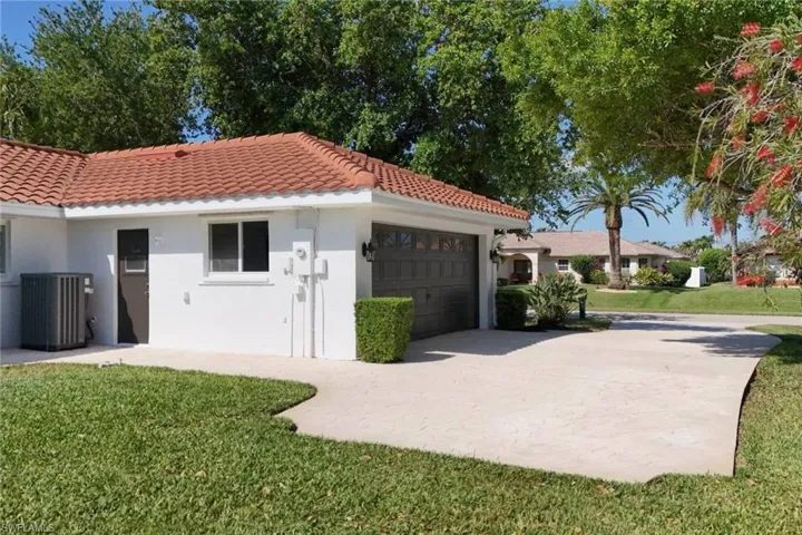 View of property exterior featuring a tile roof, driveway, cooling unit, an attached garage, and a lawn