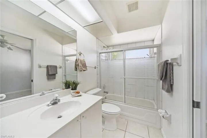 Full bath featuring vanity, toilet, tile patterned floors, visible vents, and combined bath / shower with glass door