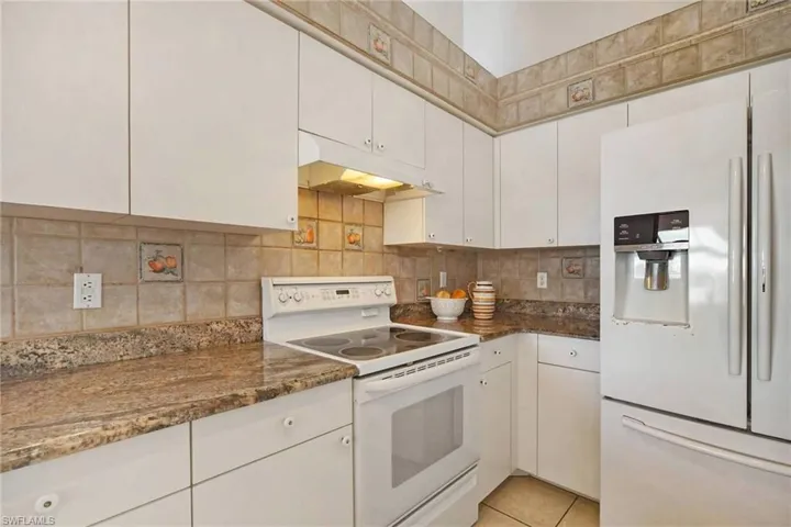 Kitchen with white cabinets, decorative backsplash, under cabinet range hood, and white appliances
