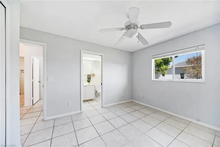 Unfurnished bedroom with light tile  flooring, ensuite bathroom, baseboards, and ceiling fan