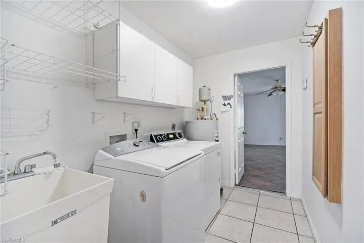 Laundry room with water heater, a sink, light tile patterned floors, washer and dryer, and cabinet space