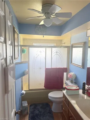 Bathroom with toilet, vanity, bath / shower combo with glass door, and a ceiling fan