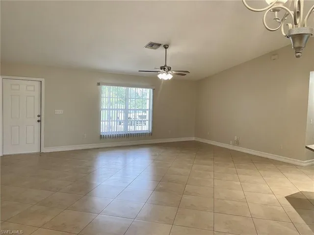 Tiled spare room featuring ceiling fan with notable chandelier and vaulted ceiling