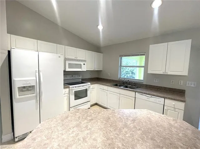 Kitchen featuring sink, lofted ceiling, white cabinets, and white appliances