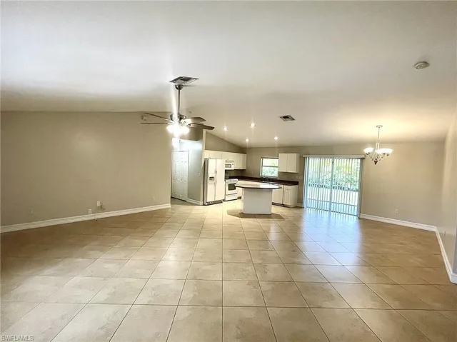 Unfurnished living room with ceiling fan with notable chandelier, lofted ceiling, and light tile patterned floors
