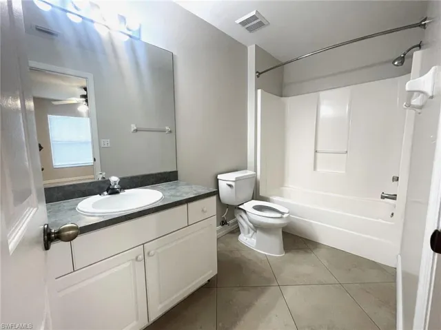 Full bathroom featuring shower / bath combination, toilet, vanity, ceiling fan, and tile patterned floors