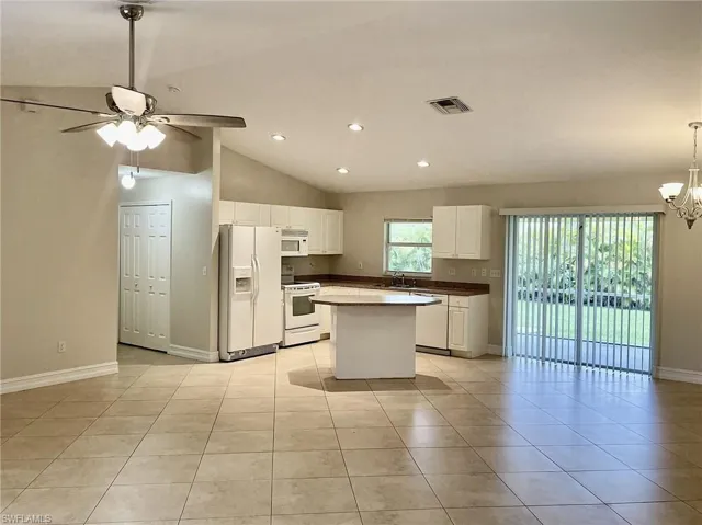 Kitchen with white cabinetry, white appliances, light tile patterned floors, ceiling fan with notable chandelier, and sink