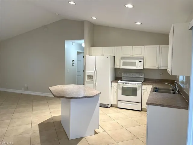 Kitchen with white cabinets, white appliances, sink, a kitchen island, and light tile patterned floors