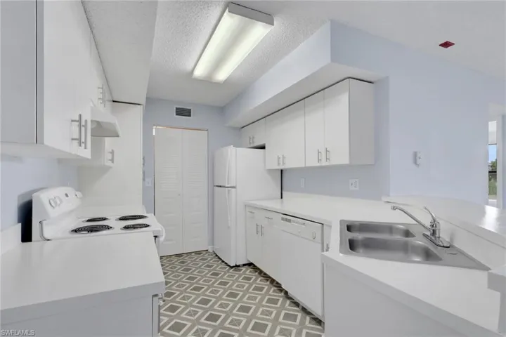 Kitchen with white cabinets, light countertops, white appliances, under cabinet range hood, and light floors