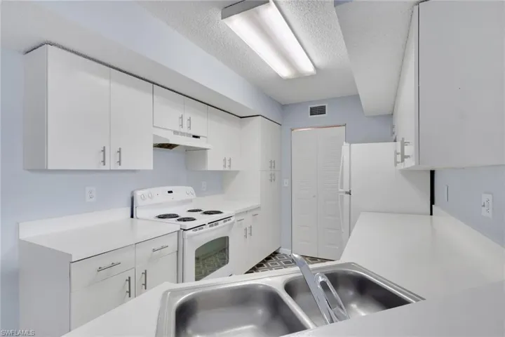Kitchen with white appliances, light countertops, white cabinets, and a textured ceiling