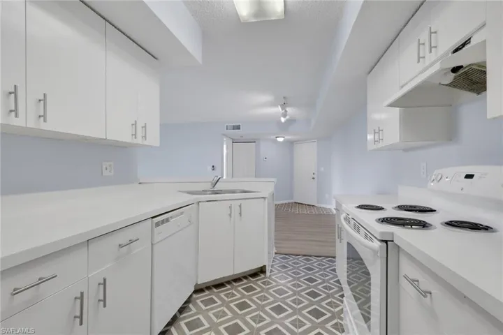 Kitchen with white appliances, light countertops, under cabinet range hood, white cabinetry, and a peninsula