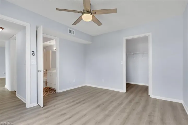 Unfurnished bedroom featuring a spacious closet, light wood-type flooring, a ceiling fan, and ensuite bathroom