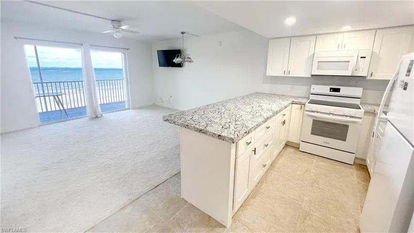 Kitchen featuring white appliances, a sink, decorative backsplash, light stone countertops, and white cabinetry