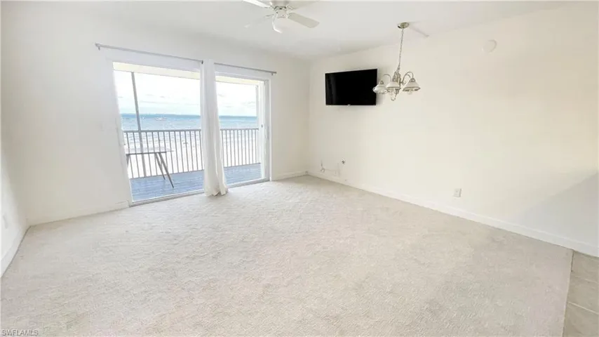 Empty room with a ceiling fan, light colored carpet, a chandelier, and baseboards