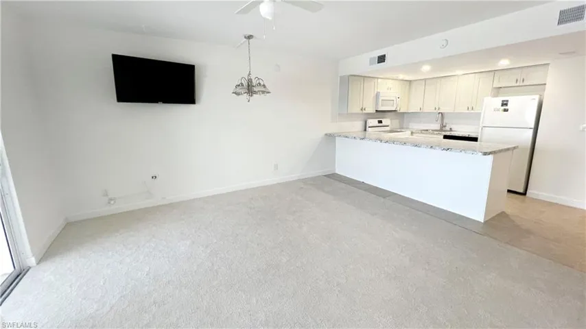 Kitchen featuring white appliances, a sink, light stone counters, baseboards, and ceiling fan