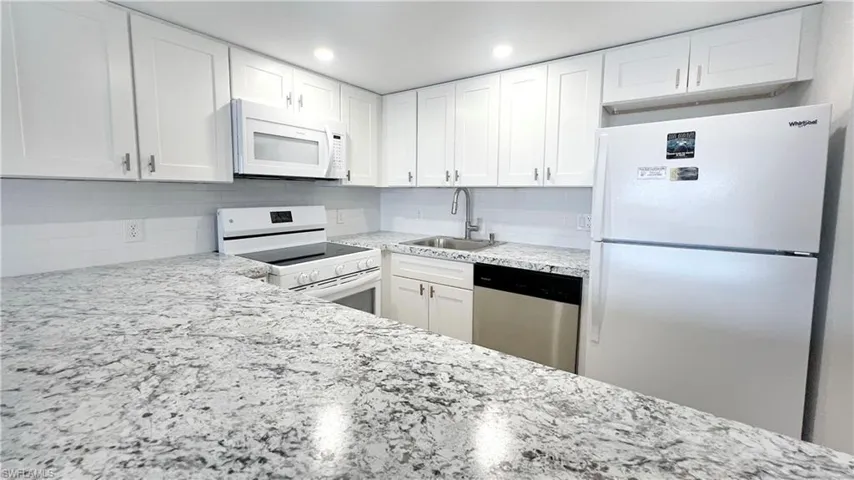 Kitchen featuring white appliances, a sink, decorative backsplash, light stone countertops, and white cabinetry