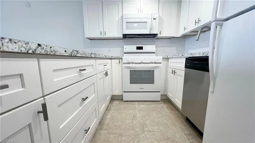 Kitchen featuring white appliances, a sink, decorative backsplash, light stone countertops, and white cabinetry