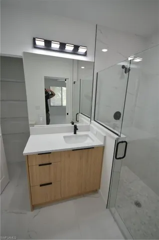 Bathroom with a marble finish shower, marble finish floor, and vanity