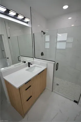 Bathroom with a marble finish shower, recessed lighting, marble finish floor, and vanity