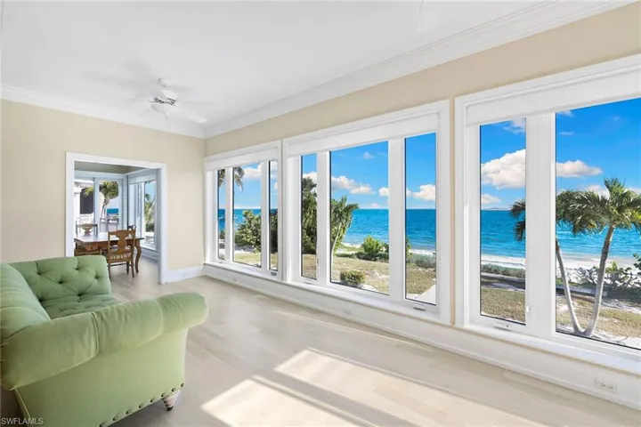 Sunroom / solarium with ornamental molding, view of water and beach, and wood finished floors