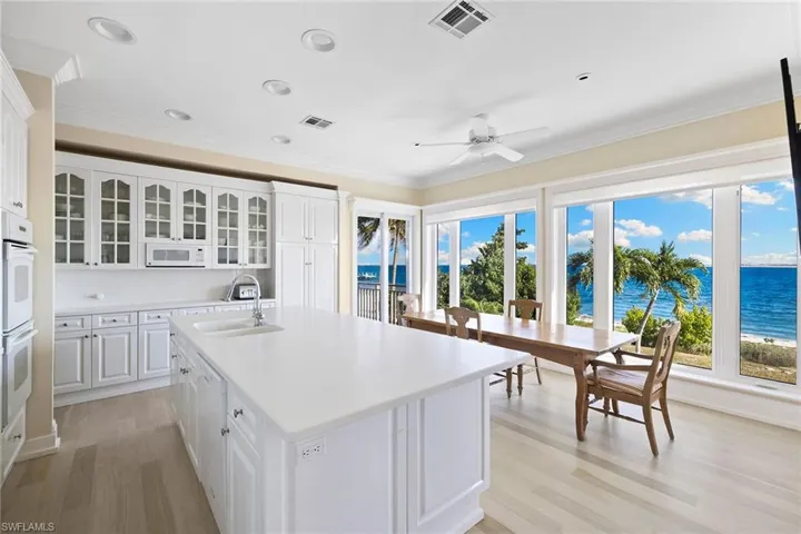 Kitchen featuring glass insert cabinets, white cabinets, crown molding, light wood-style floors, and an island with sink