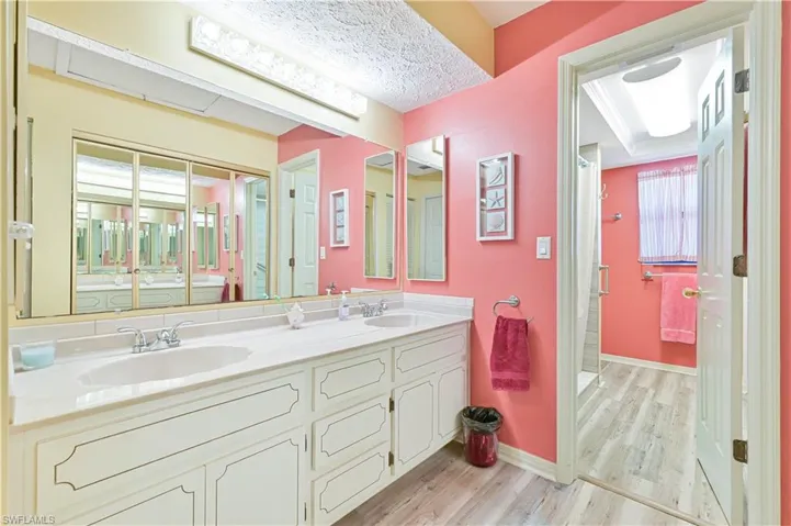 Full bathroom with double vanity, a stall shower, light wood-style flooring, and a textured ceiling