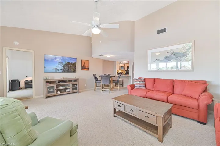 Living room featuring lofted ceiling, a ceiling fan, and light colored carpet