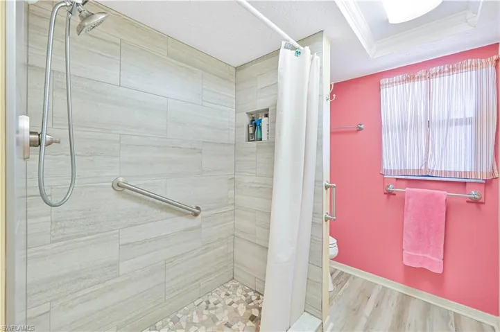 Full bathroom featuring a stall shower, light wood-type flooring, a textured ceiling, and ornamental molding