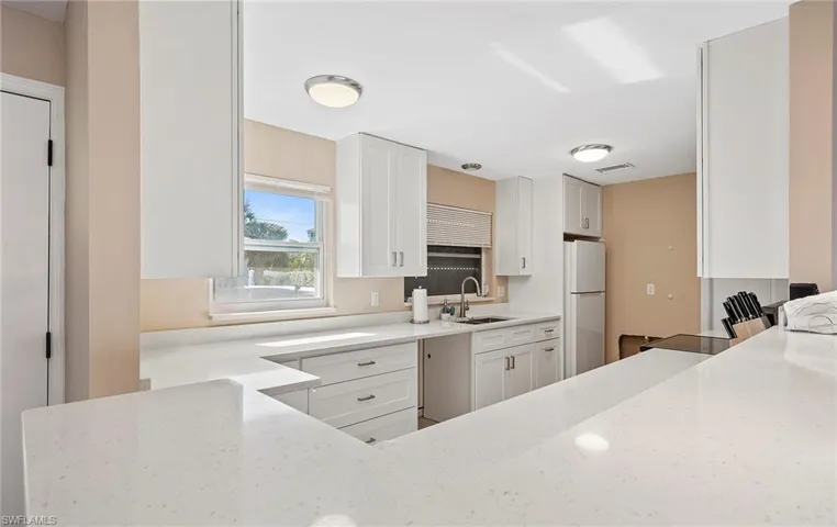 Kitchen with white fridge, sink, white cabinets, and light stone counters