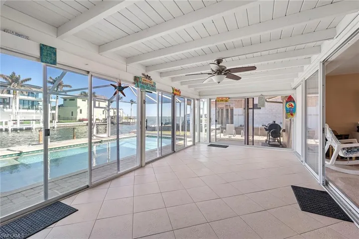 Unfurnished sunroom featuring beamed ceiling, a water view, a healthy amount of sunlight, and ceiling fan