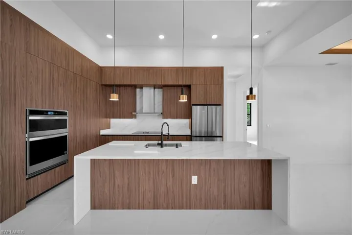 Kitchen featuring hanging light fixtures, wall chimney exhaust hood, appliances with stainless steel finishes, a large island with sink, and light tile patterned floors