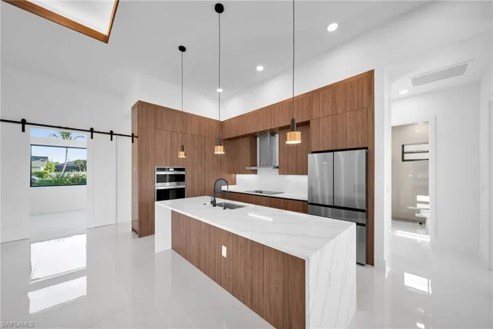 Kitchen with light tile patterned flooring, wall chimney range hood, a barn door, stainless steel appliances, and sink