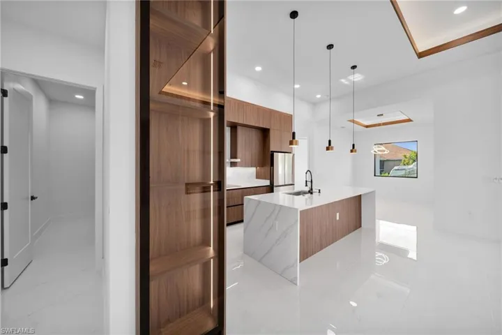 Kitchen featuring a center island with sink, sink, pendant lighting, stainless steel refrigerator, and light tile patterned floors