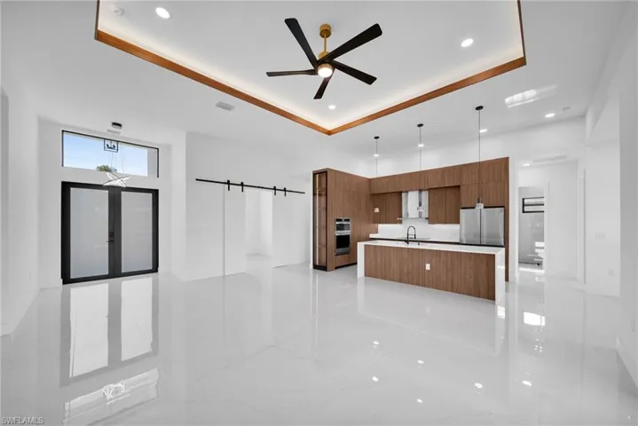 Kitchen featuring light tile patterned flooring, fridge, a tray ceiling, an island with sink, and sink