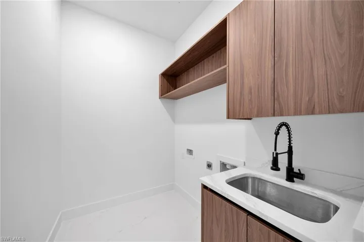 Clothes washing area with sink, cabinets, hookup for a washing machine, and light tile patterned floors