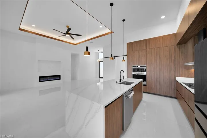 Kitchen featuring a tray ceiling, sink, decorative light fixtures, light tile patterned flooring, and ceiling fan