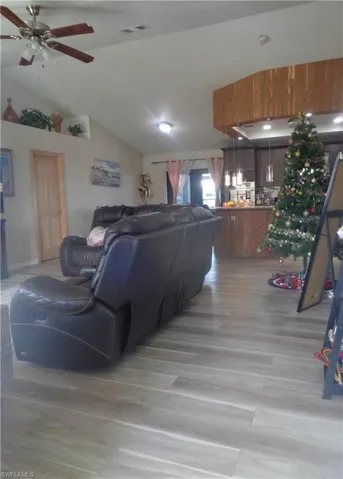Living area featuring light wood-style flooring, a ceiling fan, and vaulted ceiling