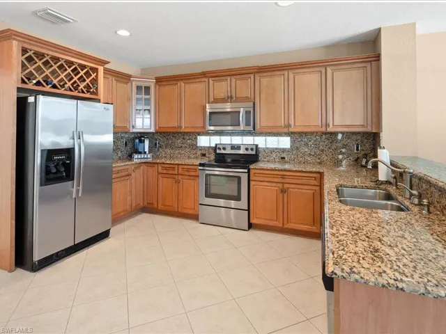 Kitchen featuring stainless steel appliances, light stone counters, backsplash, light tile floors, and sink