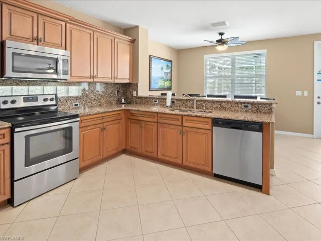 Kitchen featuring stainless steel appliances, stone countertops, sink, ceiling fan, and light tile floors