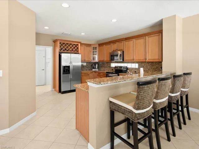 Kitchen with a kitchen breakfast bar, appliances with stainless steel finishes, kitchen peninsula, light stone counters, and tasteful backsplash