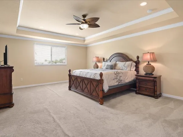 Carpeted bedroom with ceiling fan, a raised ceiling, and ornamental molding
