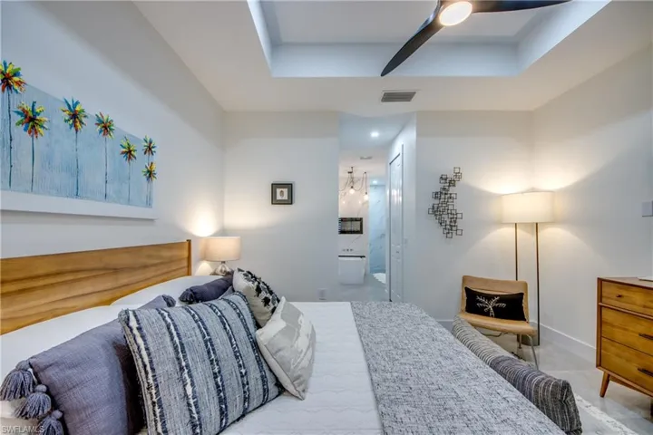 Bedroom featuring a tray ceiling, ensuite bathroom, ceiling fan, and tile floors